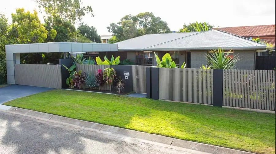 Modern home exterior with a slatted fence, lush landscaping, and a carport, showcasing space-saving design. A Grade Garage Doors, Perth