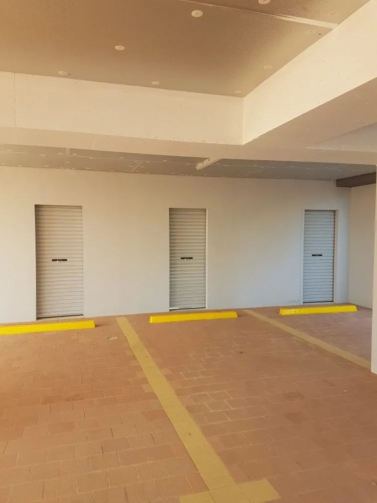 Three closed roll-up garage doors in a parking area with yellow parking stops. A Grade Garage Doors, Perth